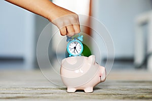 Time is precious, save time concept with piggy bank and blue alarm clock in little girl hand