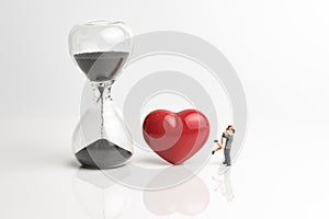 Time prove love for couple concept, with sandglass or hourglass, red shiny ceramic heart shape and miniature couple holding each