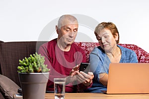 Time in quarantine. An older couple sitting at home with a computer and phone