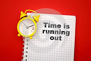 Time is Running Out - phrase on notebook with yellow alarm clock aside on red background