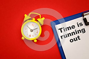 Time is Running Out - phrase on paper with yellow alarm clock aside on red background