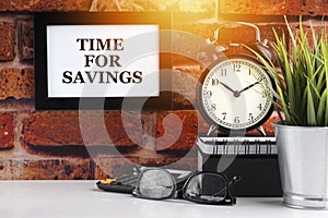 TIME FOR SAVINGS text with alarm clock, books and vase on brick background