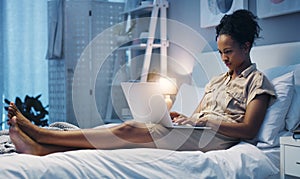 Time for some late night blogging. Shot of an attractive young woman using her laptop while lying on her bed after a