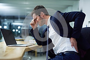 Time for some lumbar support. Shot of a businessman wincing in pain and holding his lower back while sitting at a desk