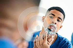 Time to be clean shaven for a while again. a focused young man checking his reflection as he shaves his face.