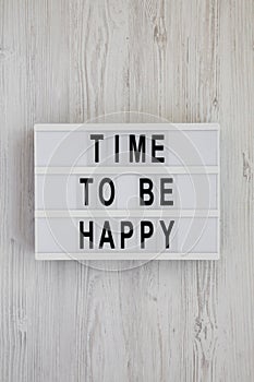 `Time to be happy` words on a lightbox on a white wooden background, top view. Overhead, from above. Flat lay. Close-up