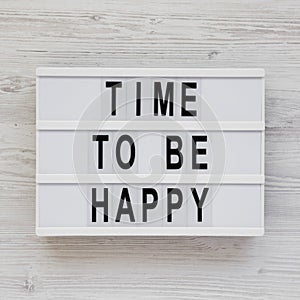 `Time to be happy` words on a lightbox on a white wooden background, top view. Overhead, from above. Flat lay. Close-up