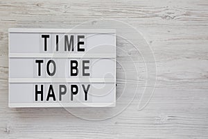 `Time to be happy` words on a lightbox on a white wooden background, top view. Overhead, from above. Flat lay. Copy space