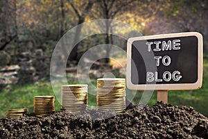 Time To Blog concept. Golden coins in soil Chalkboard on blurred natural background