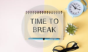 TIME TO BREAK is written in a notebook on a workplace near a flower, a diary and a calculator.