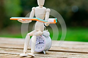time to brush your teeth concept. Toothbrush in the hands of a human figurine and an alarm clock