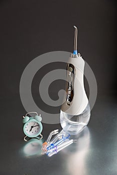 Time to brush your teeth. Oral irrigator and an alarm clock on a black background