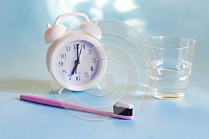 time to brush your teeth. toothbrush with toothpaste watch and glass of water on a blue background