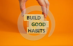 Time to build good habits. Wooden blocks with words `build good habits`. Beautiful orange background, male hand. Copy space.