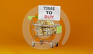 Time to buy real estate symbol. Miniature shopping cart with wooden houses, words time to buy. Beautiful orange background, copy