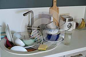 Time to clean: A daunting stack of soiled plates, bowls, and utensils fills the sink, accompanied by a sponge for