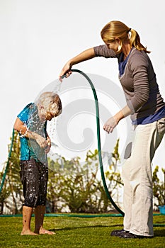 Time to clean off some of that dirt....Little boy getting wet by his mother with a hose pipe.