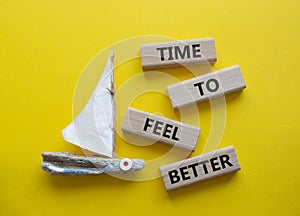 Time to feel better symbol. Wooden blocks with words Time to feel better. Beautiful yellow background with boat. Medicine and Time