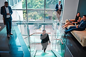 Time to get down to business. a young businesswoman walking up the stairs while using a phone in a busy office at work.