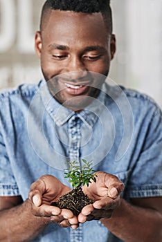 Time to get growing with your new business. a young man holding a plant growing out of soil in a modern office.