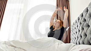 Time to get ready. Young curvy woman in black T shirt stretching, waking up happily after a good night sleep