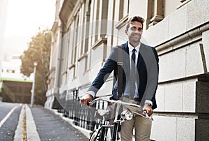 Time to get to work. Shot of a handsome young businessman pushing his bicycle while making his way to work in the