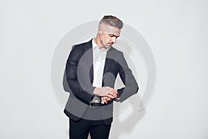 Time to go. Handsome bearded businessman in classic suit looking at watch on his hand while standing against grey