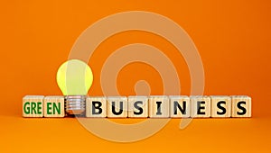 Time to green business symbol. Wooden cubes with words `Green business`. Yellow light bulb. Beautiful orange background. Green