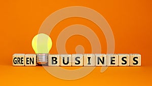 Time to green business symbol. Wooden cubes with words `Green business`. Yellow light bulb. Beautiful orange background. Green