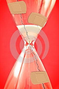 Time to heal - concept image with cracked hourglass and bandaid on red background