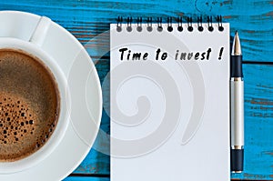 Time to invest - notice in notepad at blue wooden table with morning coffee mug. Savings, Money business concept