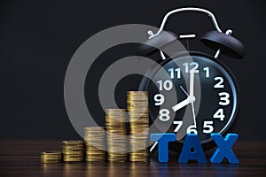 Time to pay TAX concept. TAX alphabet with stack of coin and vintage alarm clock in dark background, business and financial