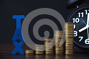 Time to pay TAX concept. TAX alphabet with stack of coin and vintage alarm clock in dark background, business and financial