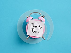 Time to plan ideas, reconsider and evaluate events or actions concept. Pink alarm clock with a note paper on blue background with