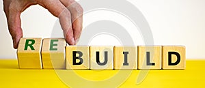Time to rebuild. Businessman turns wooden cubes and changes the word build to rebuild on a beautiful yellow table, white