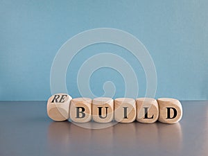 Time to rebuild. Concept words build and rebuild on cubes on a beautiful blue background. Grey table. Business concept.