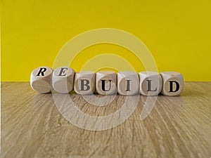 Time to rebuild. Concept words build and rebuild on cubes on a beautiful yellow background. Wooden table. Business concept.