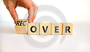 Time to recover symbol. Businessman turns a wooden cube and changes the word `over` to `recover`. Beautiful white table, white