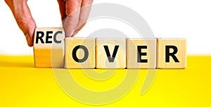 Time to recover symbol. Businessman turns a wooden cube and changes the word `over` to `recover`. Beautiful yellow table, whit