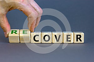 Time to recover symbol. Businessman turns wooden cubes and changes the word `cover` to `recover`. Beautiful grey background.