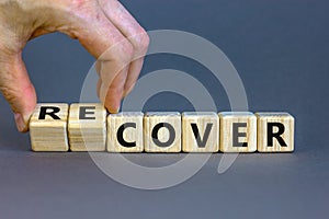 Time to recover symbol. Businessman turns wooden cubes and changes the word `cover` to `recover`. Beautiful grey background.