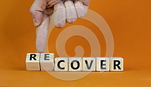 Time to recover symbol. Businessman turns wooden cubes and changes the word `cover` to `recover`. Beautiful orange background.