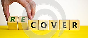 Time to recover symbol. Businessman turns wooden cubes and changes the word `cover` to `recover`. Beautiful yellow table, whit