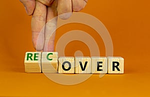 Time to recover symbol. Businessman turns wooden cubes and changes the word `over` to `recover`. Beautiful orange table, orang