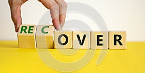 Time to recover symbol. Businessman turns wooden cubes and changes the word `over` to `recover`. Beautiful yellow table, white
