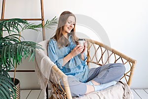 Time to relax. Smiling girl drinking hot coffee from paper cup sits in wicker