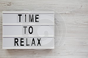 `Time to relax` words on a modern board on a white wooden background, top view. Overhead, from above. Flat lay. Copy space