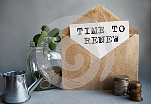 TIME TO RENEW text is written on white paper on an antique envelope, which lies on the table along with a stack of coins, a glass