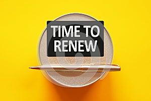 TIME TO RENEW - words on a black sheet on a yellow background with round metal stand and metal writing pen. Business, finance and