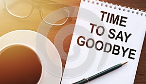 Time to say goodbye text. A concept that means a moment of separation from something. Notepad on a wooden table with a cup of